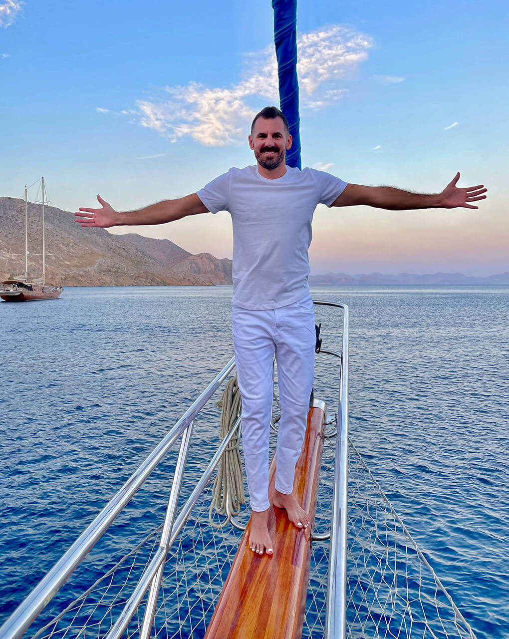 Cory standing on the bowsprit of a sailboat with his arms out