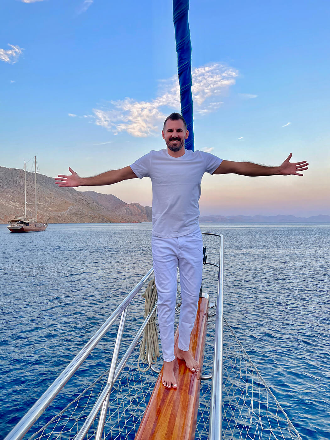 Cory standing on the bowsprit of a sailboat with his arms out