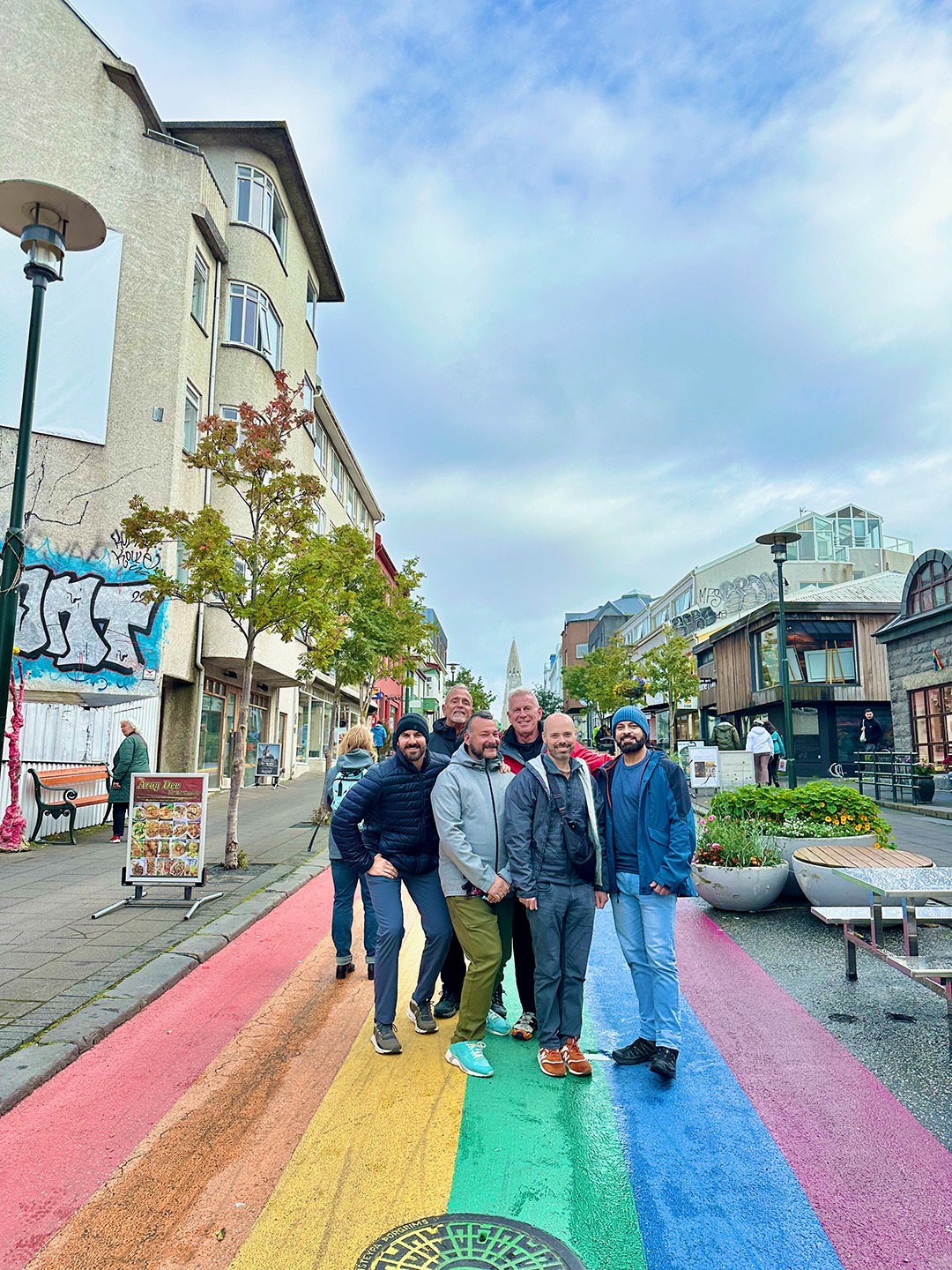 LGBTQ safe and inclusive travel with Pivot Trip - group of gay men travelers stand on rainbow colored road