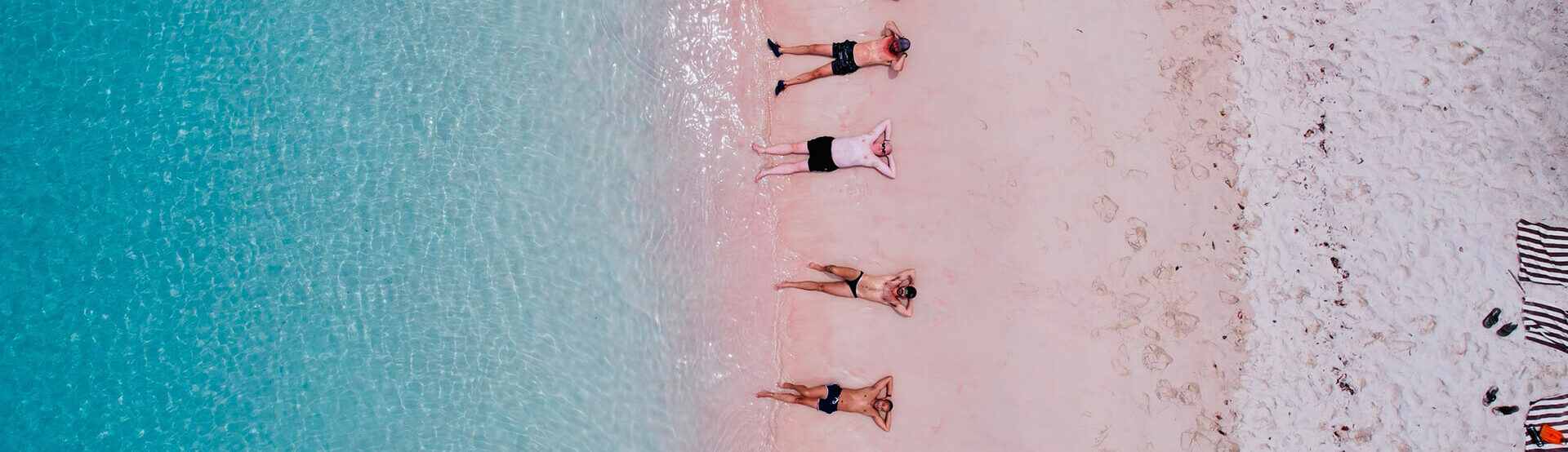 men lying on pink sand beach with turquoise water