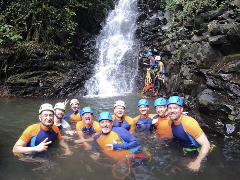 A group of gay men on an adventure in front of a waterfall