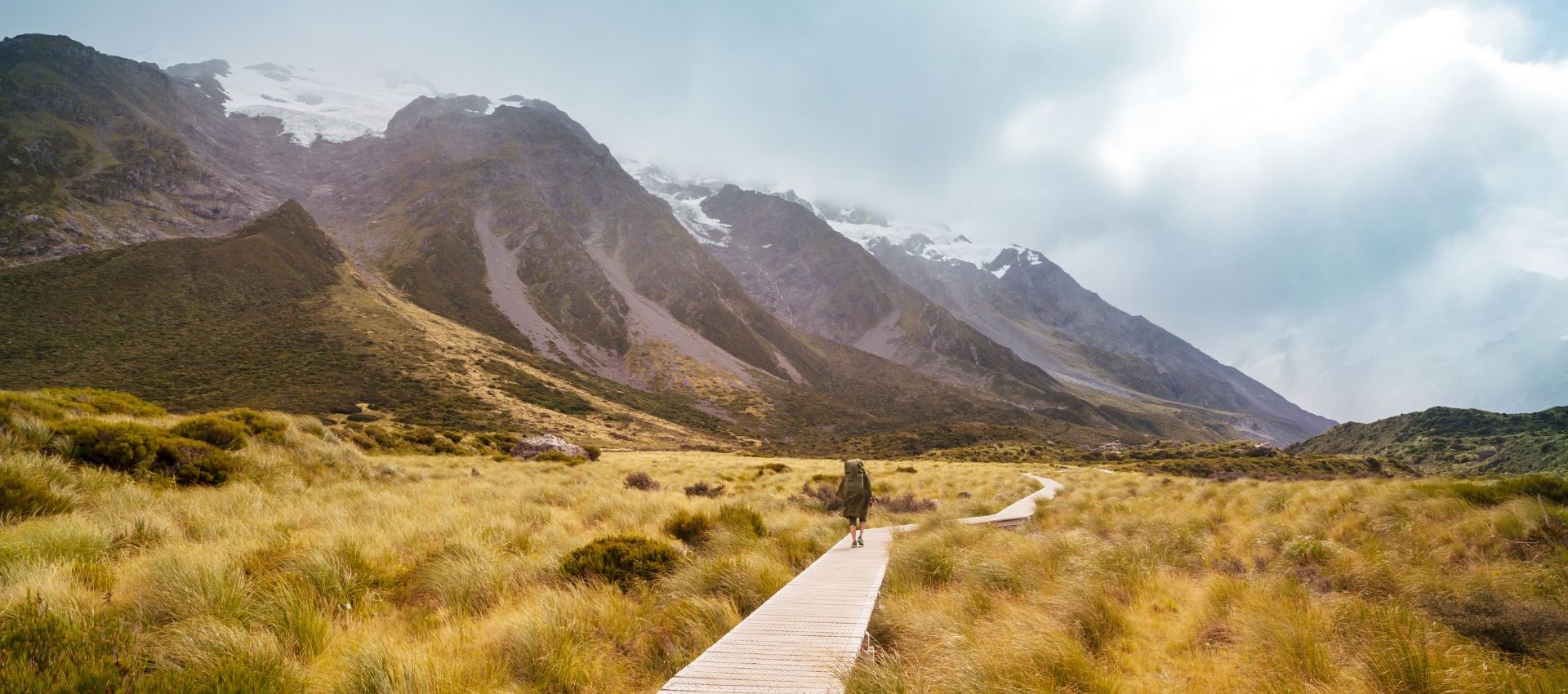 New Zealand South Island man walking in valley with mountains in background - gay tour of new zealand - pivot trip